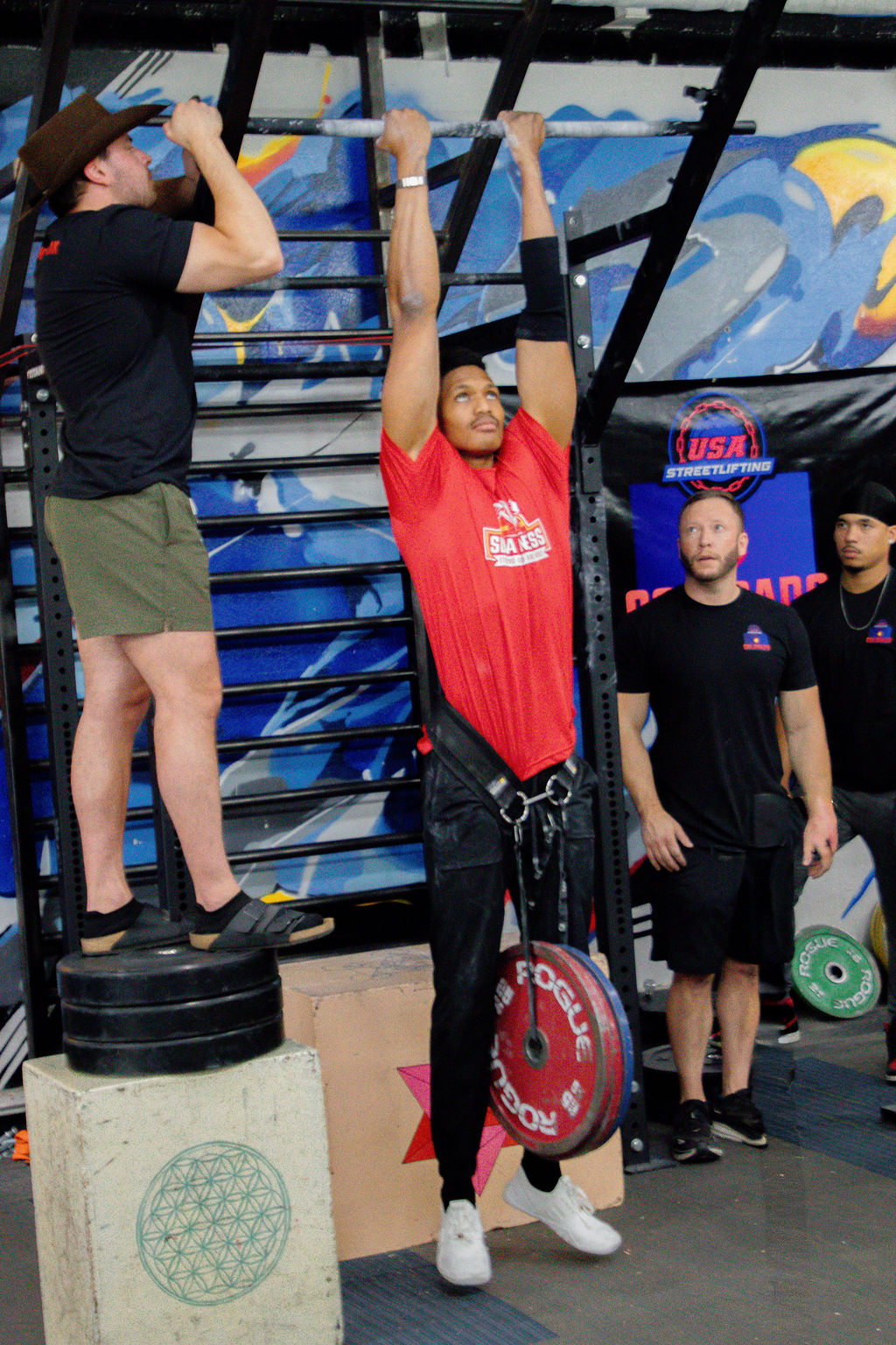 Shai Ariola competing in a weighted pull-up at a streetlifting competition